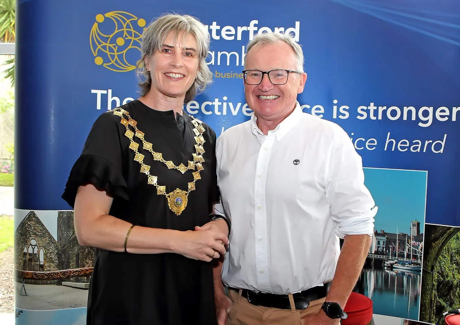 Two people smiling in front of a Waterford Chamber banner at a Chamber event
